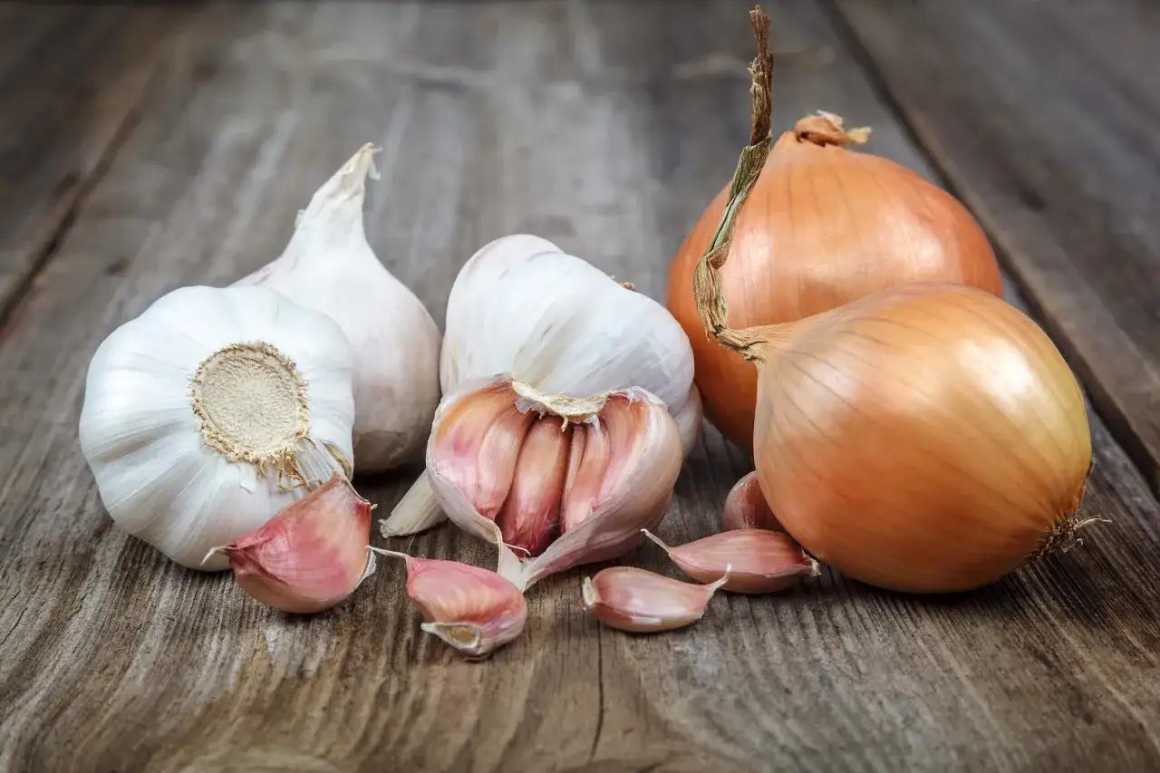 Aglio e cipolle sul legno. Per sapere come togliere l'odore di aglio dalla bocca, questi ingredienti sono un buon punto di partenza.