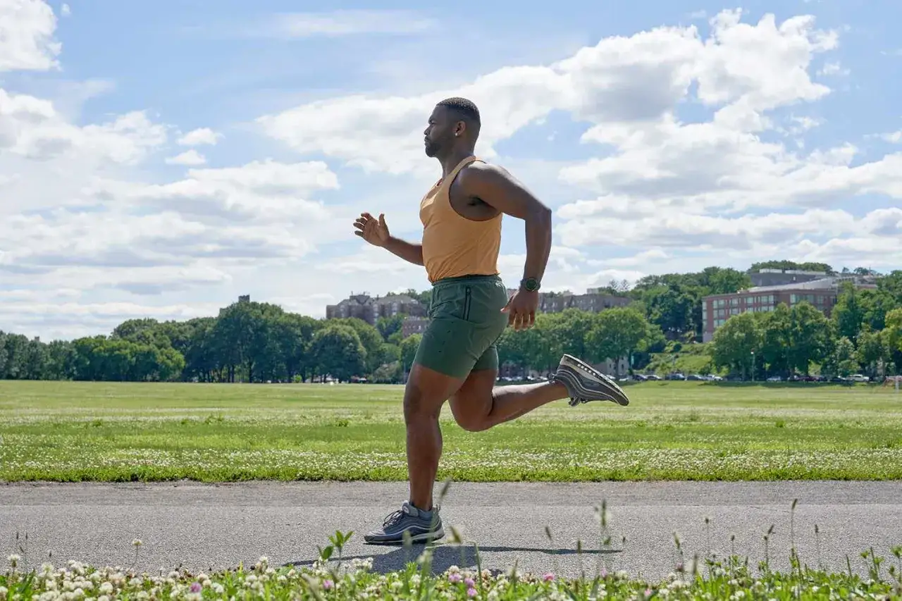 Mann im Laufoutfit beim intensiven HIT Training im Park, mit gr&uuml;ner Wiese und blauen Himmel.