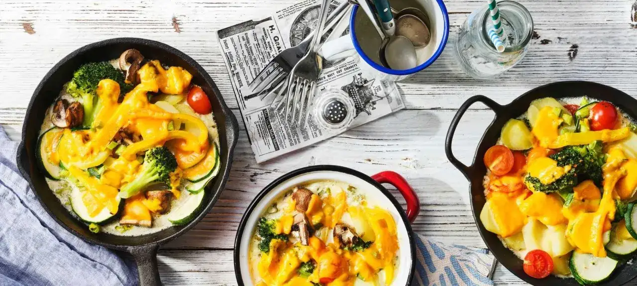 Leckere Raclette Ideen: Gem&uuml;se mit geschmolzenem K&auml;se in Pfannen. Perfekt f&uuml;r gem&uuml;tliche Abende!