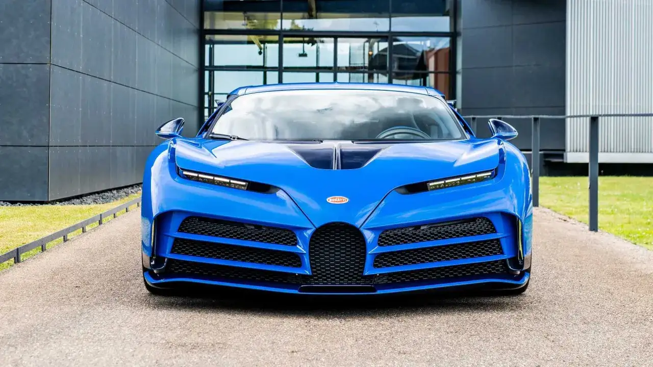 Niebieski Bugatti Centodieci z charakterystycznym grillem i ostrymi liniami, zaparkowany przed nowoczesnym budynkiem.