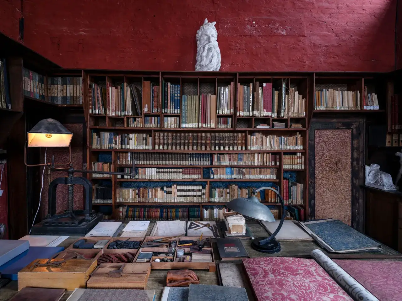 Scrivania e scaffali pieni di libri nel museo Palazzo Fortuny, con una statua in cima.