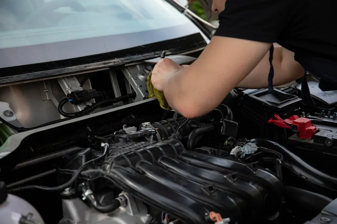 Mechanik sprawdza, dlaczego rozrusznik nie kręci tylko cyka. Widać elementy silnika i akumulator.