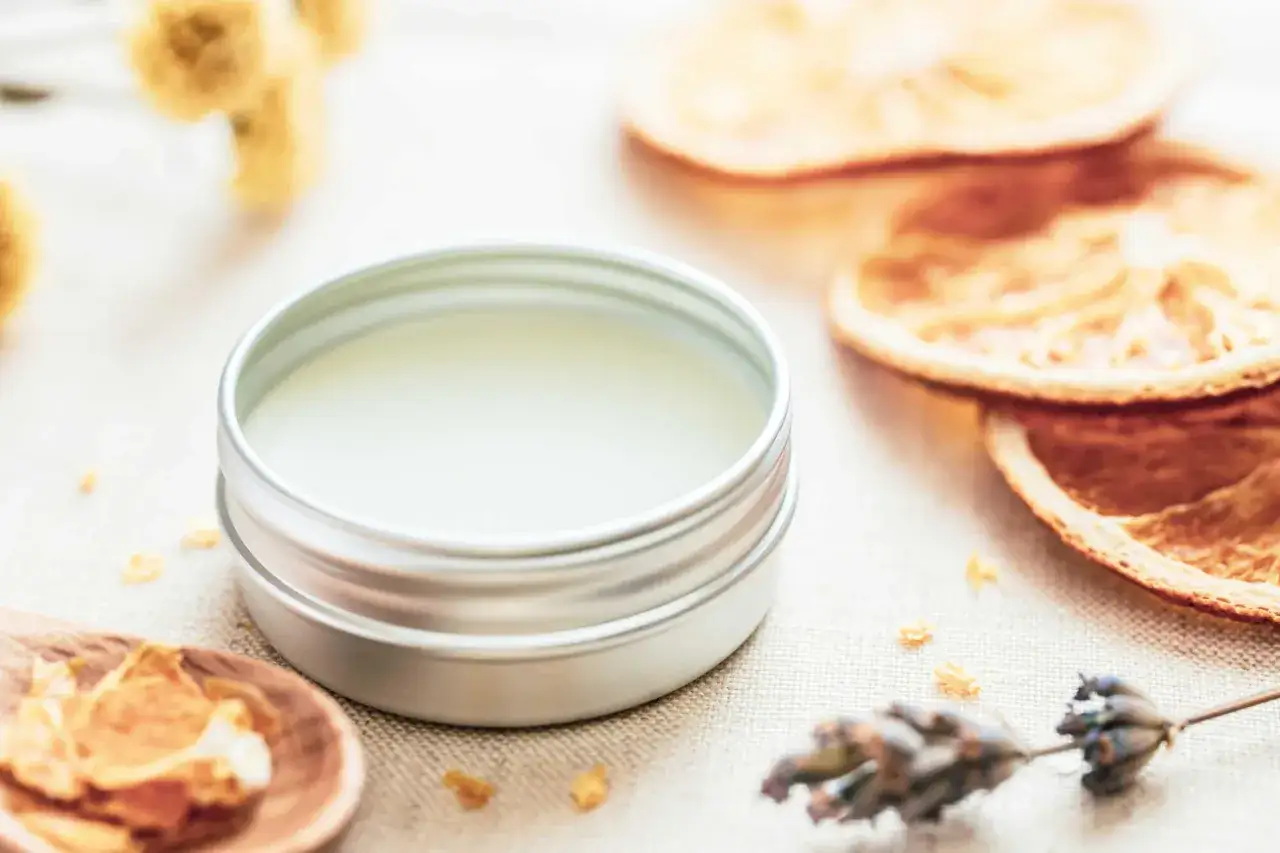 Ein Döschen mit selbstgemachtem Lippenbalsam, umgeben von getrockneten Orangen, Lavendel und Kräutern.