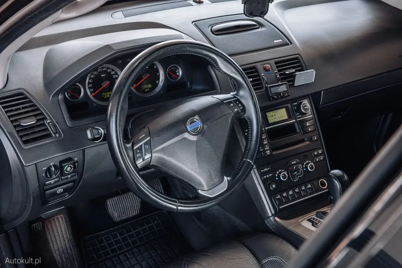 Wnętrze Volvo XC90 V8: kierownica, deska rozdzielcza z radiem i nawigacją, zegary.