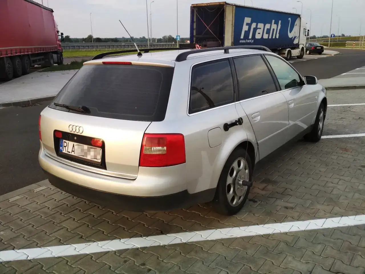 Srebrne Audi A6 C5 2.5 TDI na parkingu. W tle ciężarówka Fracht i czarny samochód.