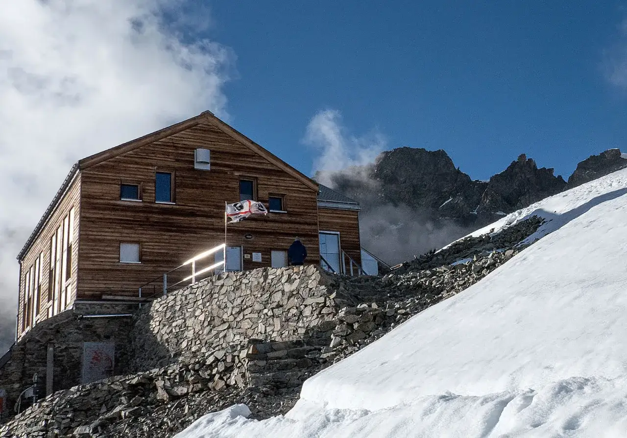 Il rifugio Marinelli, un edificio in legno su un pendio innevato, con rocce e montagne sullo sfondo.