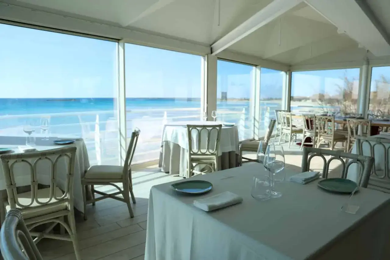 Tavoli apparecchiati con vista sul mare a Porto Cesareo. L'atmosfera &egrave; rilassata, perfetta per godersi il panorama.