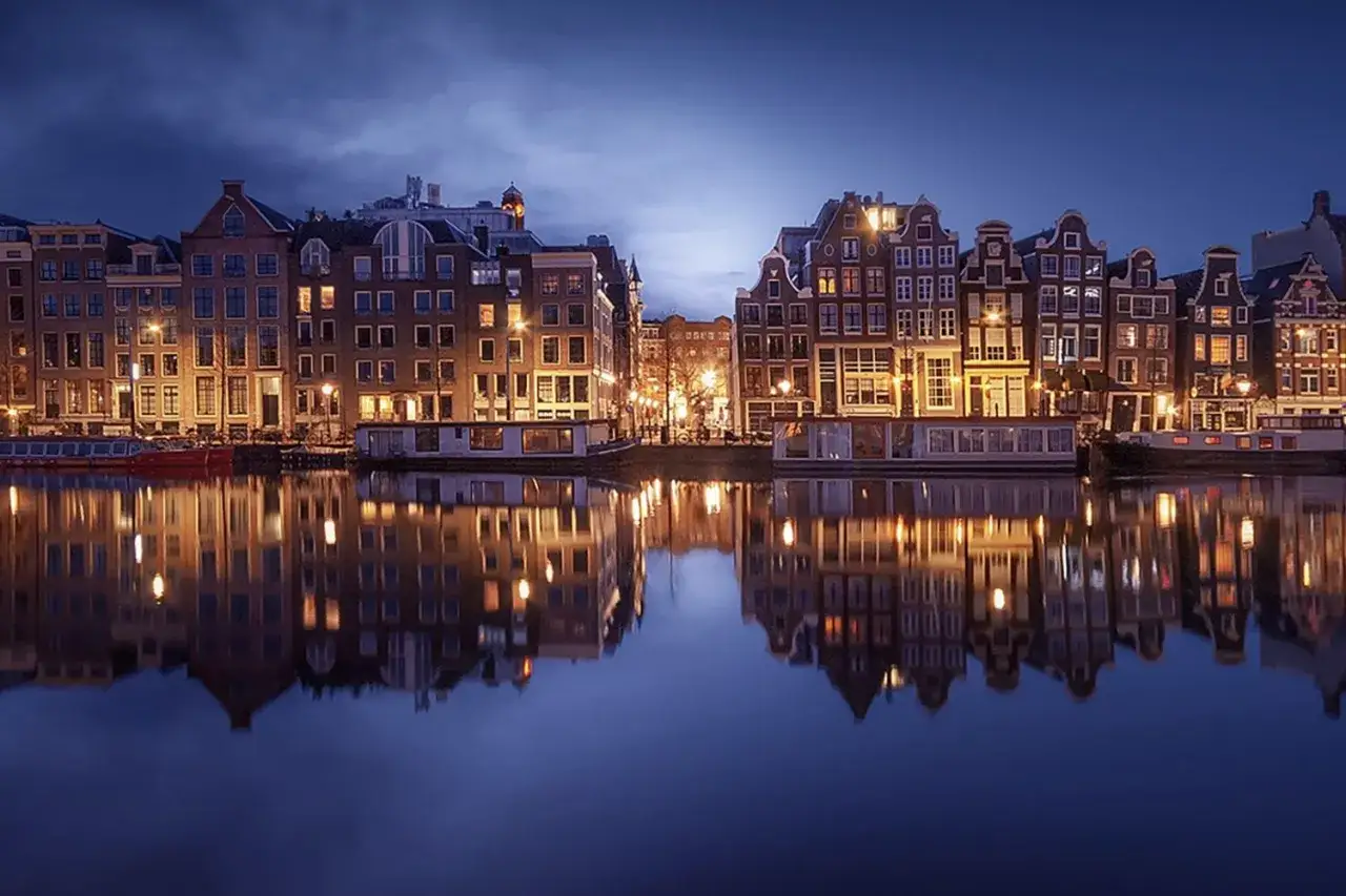 Amsterdamskie kamienice odbijają się w spokojnej wodzie podczas magicznej niebieskiej godziny.