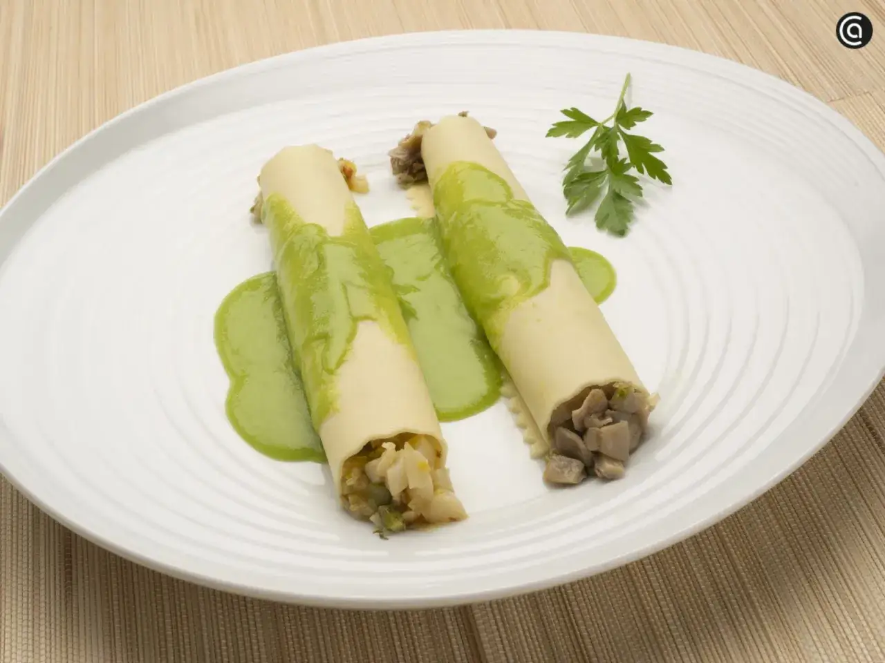 Dos canelones de verano rellenos de verduras y carne, ba&ntilde;ados en una cremosa salsa verde y decorados con perejil.