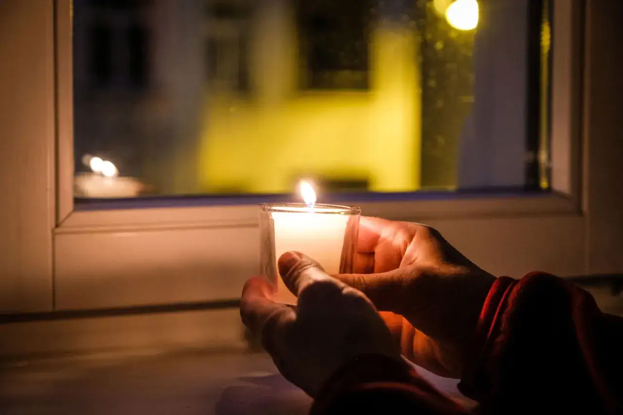 H&auml;nde halten eine Kerze am Fenster. Ein Licht der Hoffnung, wie in Psalm 128, erhellt die Dunkelheit.