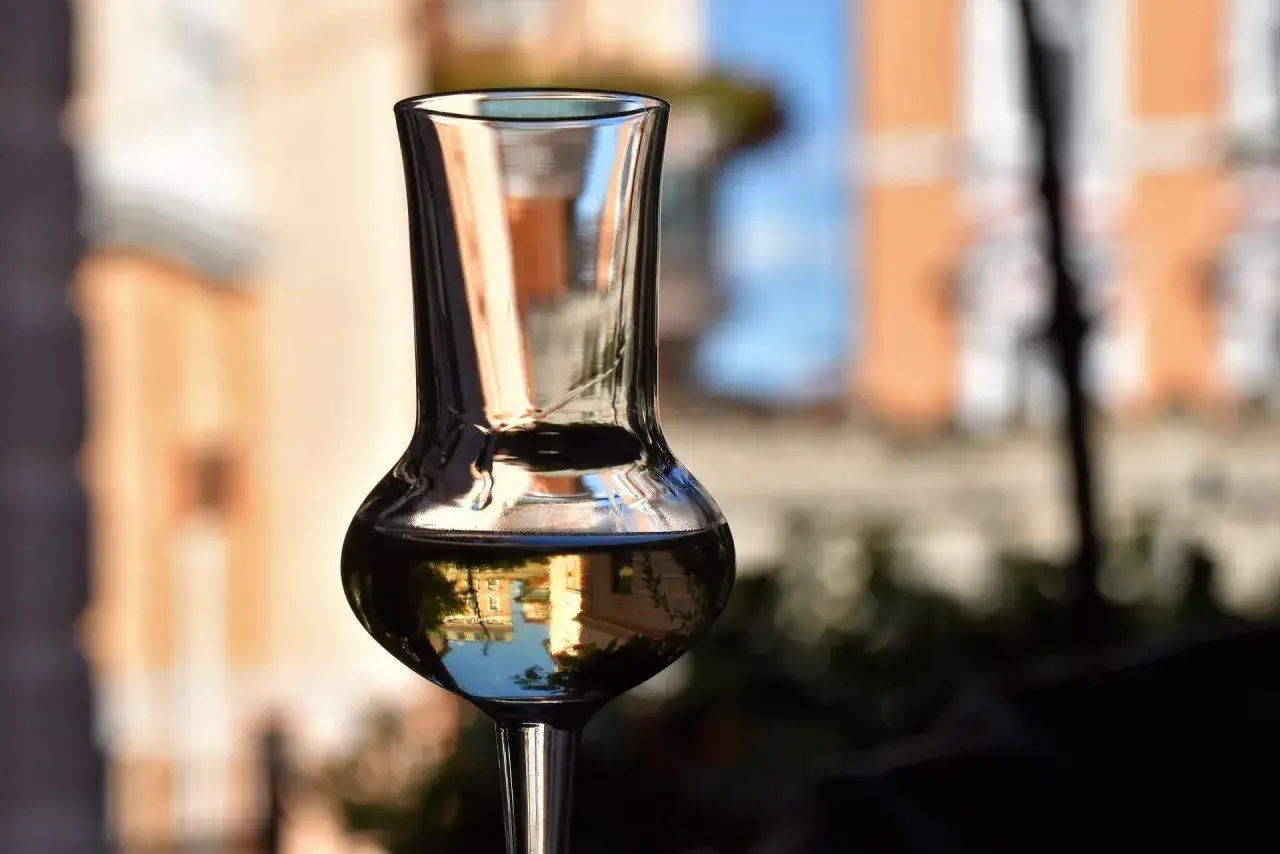 Ein Glas klarer Flüssigkeit, vielleicht Kartoffelschnaps selber machen, spiegelt Gebäude und Himmel.