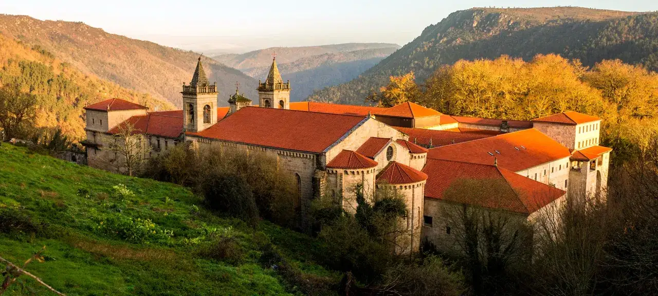 Majestuoso conjunto de monasterios de Galicia, con tejados rojos y torres, rodeado de colinas boscosas al atardecer.