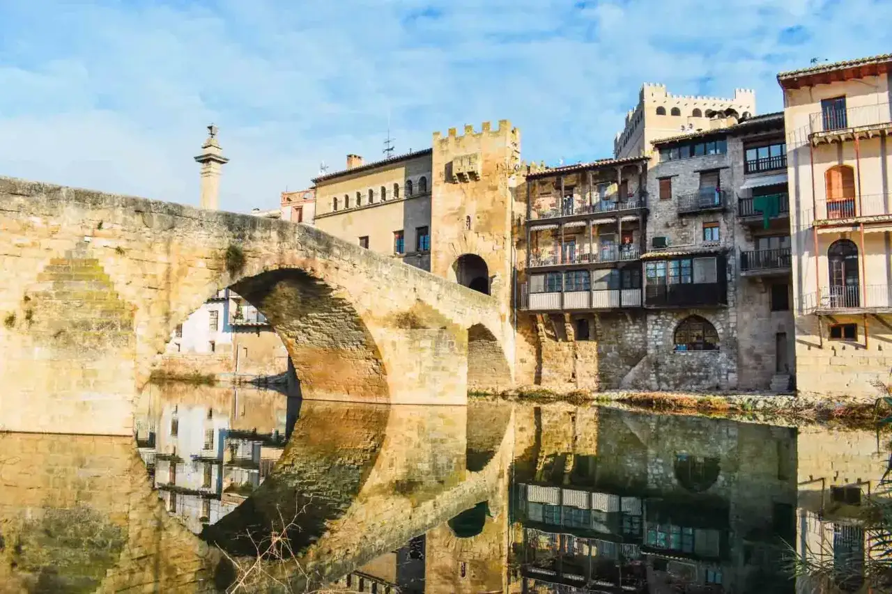 Puente medieval y casas colgantes reflejadas en el río, un rincón que evoca la toscana española.