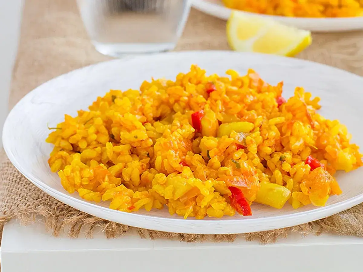 Un plato de arroz con verduras, con trozos de pimiento rojo y amarillo, servido en una vajilla blanca.