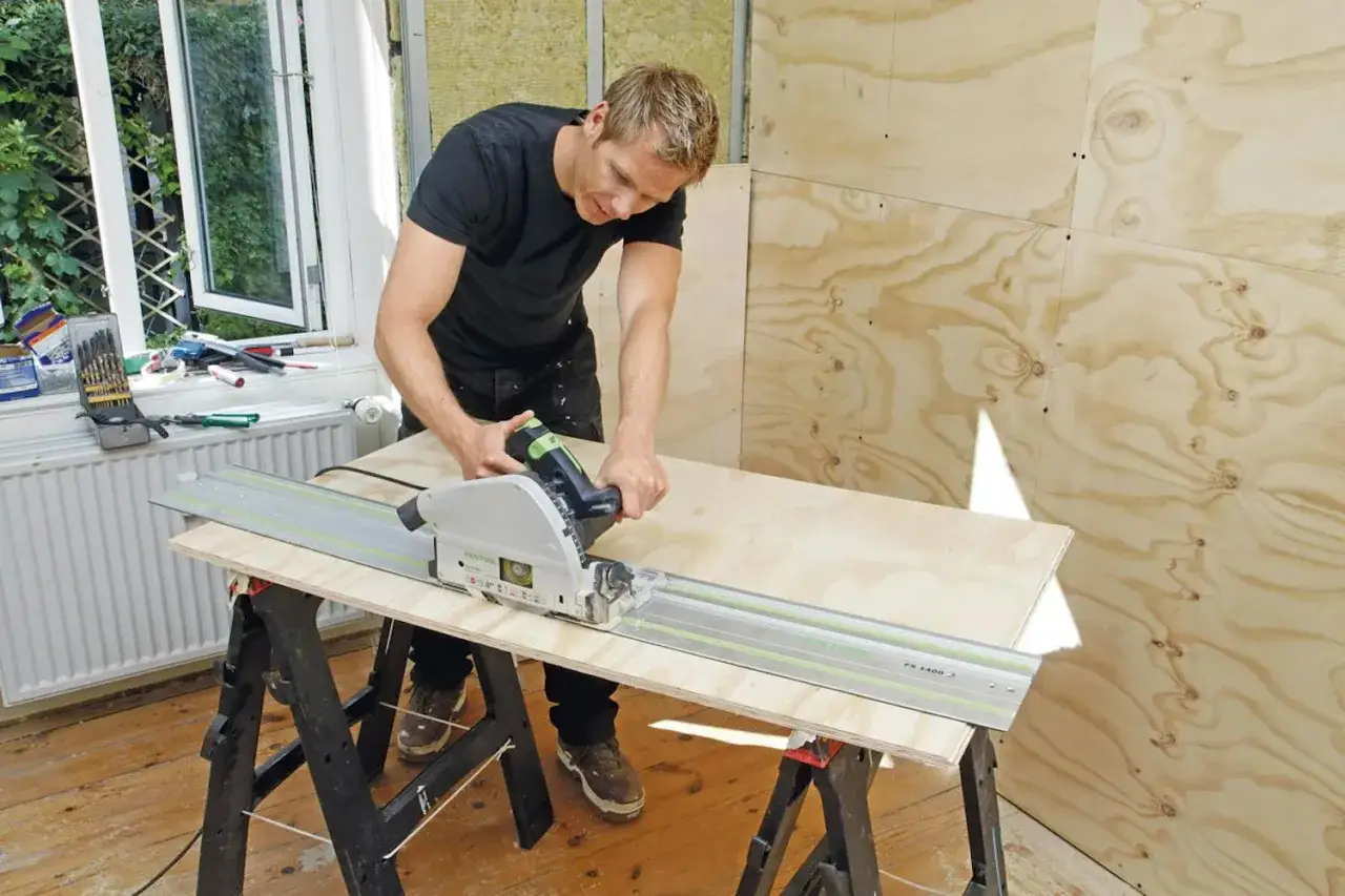 Man spacklar plywood med en cirkelsåg på en skena.