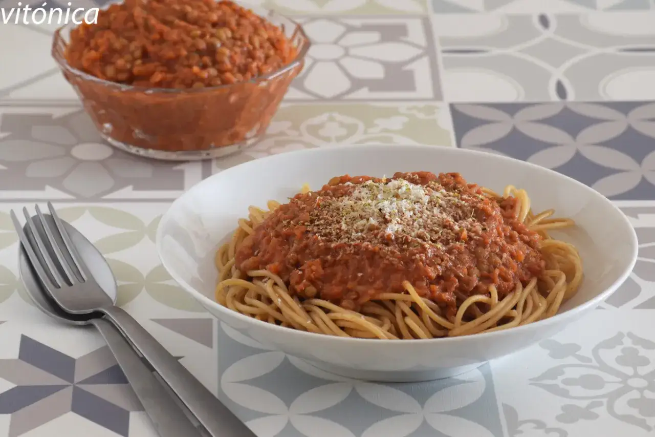 Plato de espaguetis con boloñesa de lentejas, espolvoreado con queso rallado y hierbas. Un bol con más salsa al fondo.