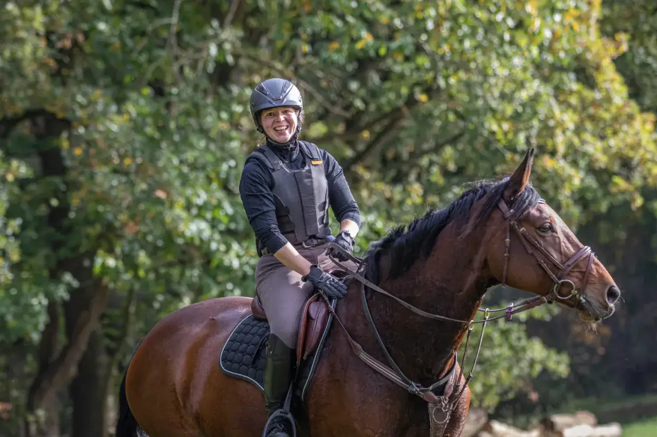 Glückliche Reiterin genießt das **trail reiten** auf einem braunen Pferd im Wald.