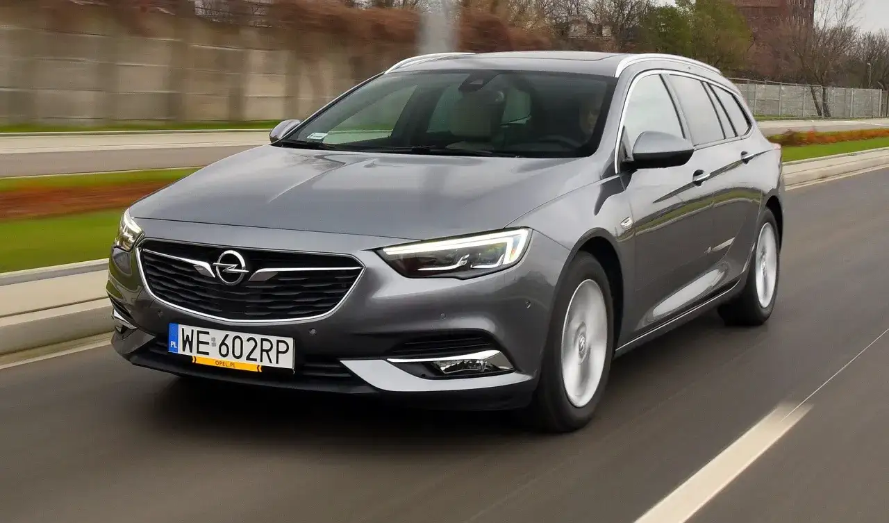 Szary Opel Insignia 1.6 Turbo kombi jedzie po drodze, widać rozmyte tło.