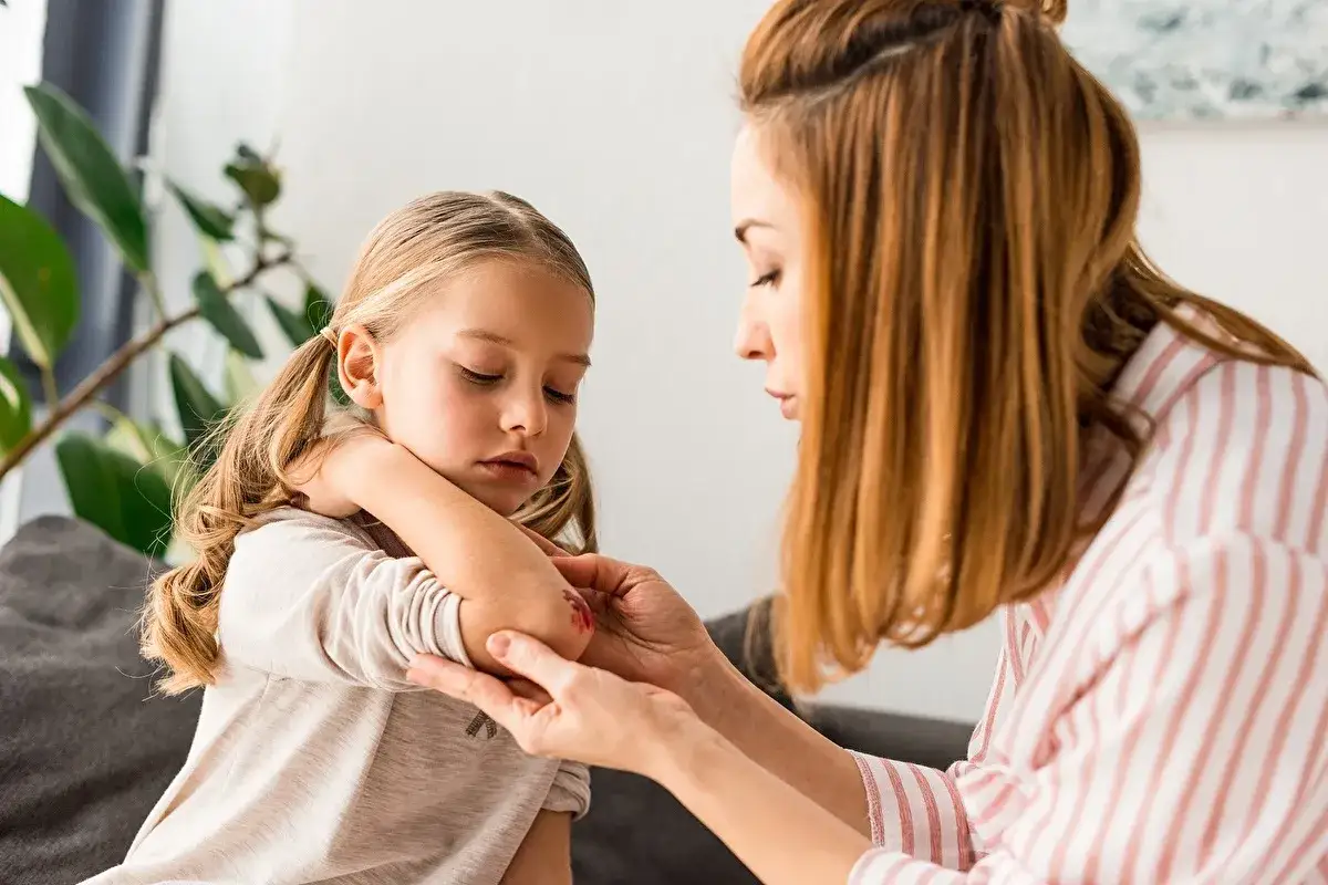 Une femme examine le coude blessé d'une jeune fille. Savoir que faire en cas d'accident en centre de loisirs est essentiel.