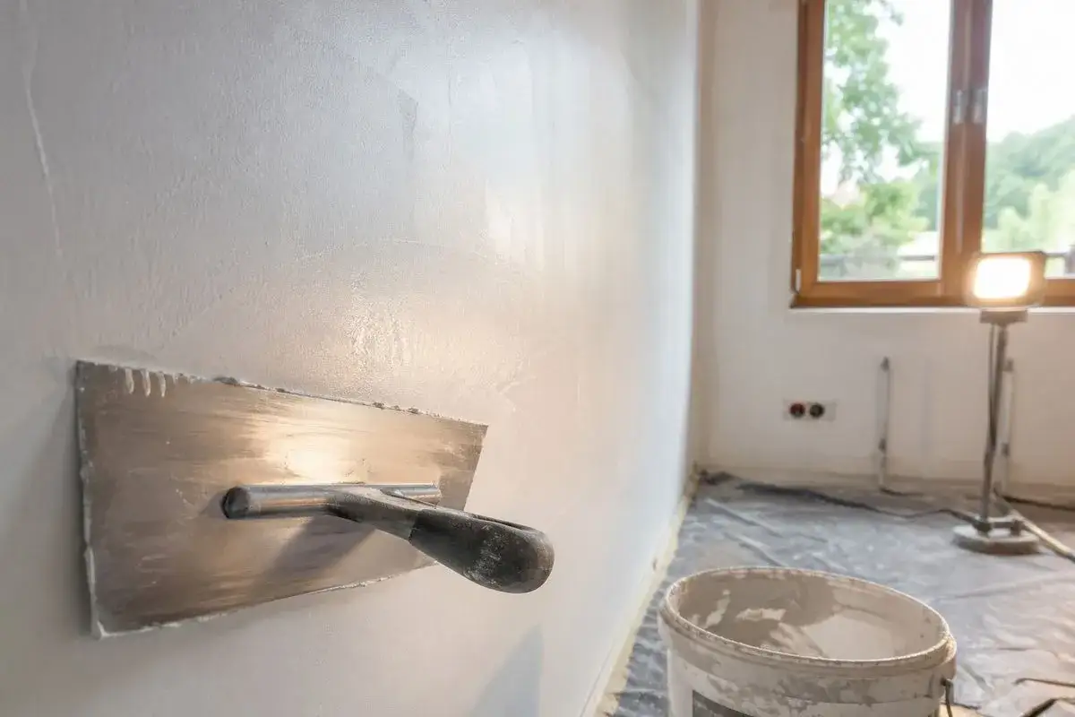 Gładź nakładana kielnią na ścianę, przygotowanie pod malowanie. R&oacute;żnica między tynkiem a gładzią jest widoczna.
