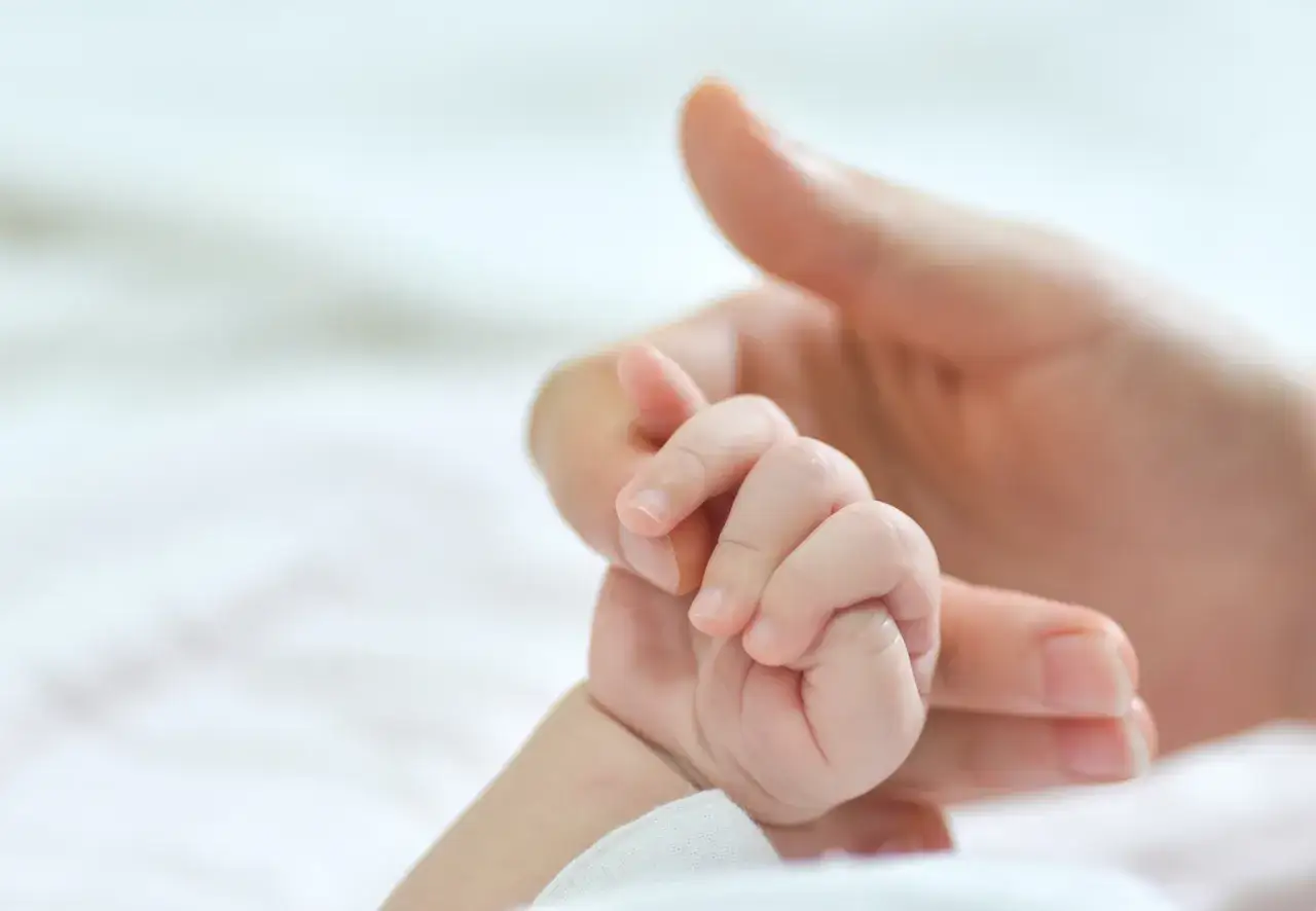 Dłoń rodzica obejmuje maleńką rączkę dziecka. To symbol miłości i troski, a także obietnica wsparcia, jak becikowe dla kogoś, kto dopiero zaczyna swoją drogę.