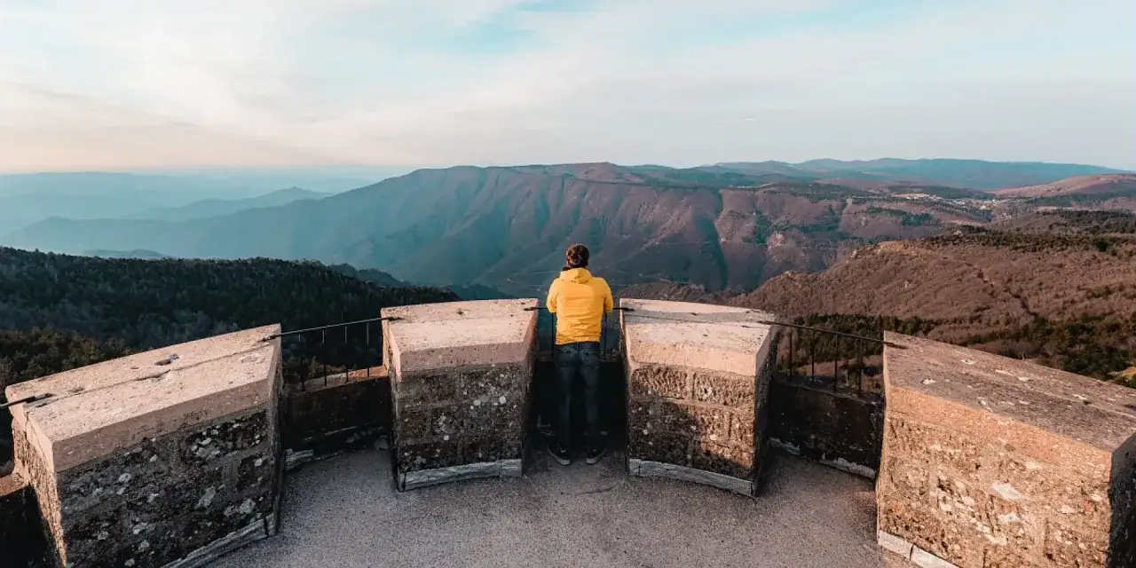 Un homme en jaune admire le panorama depuis le sommet du Mont Aigoual, contemplant les montagnes bleutées à perte de vue.