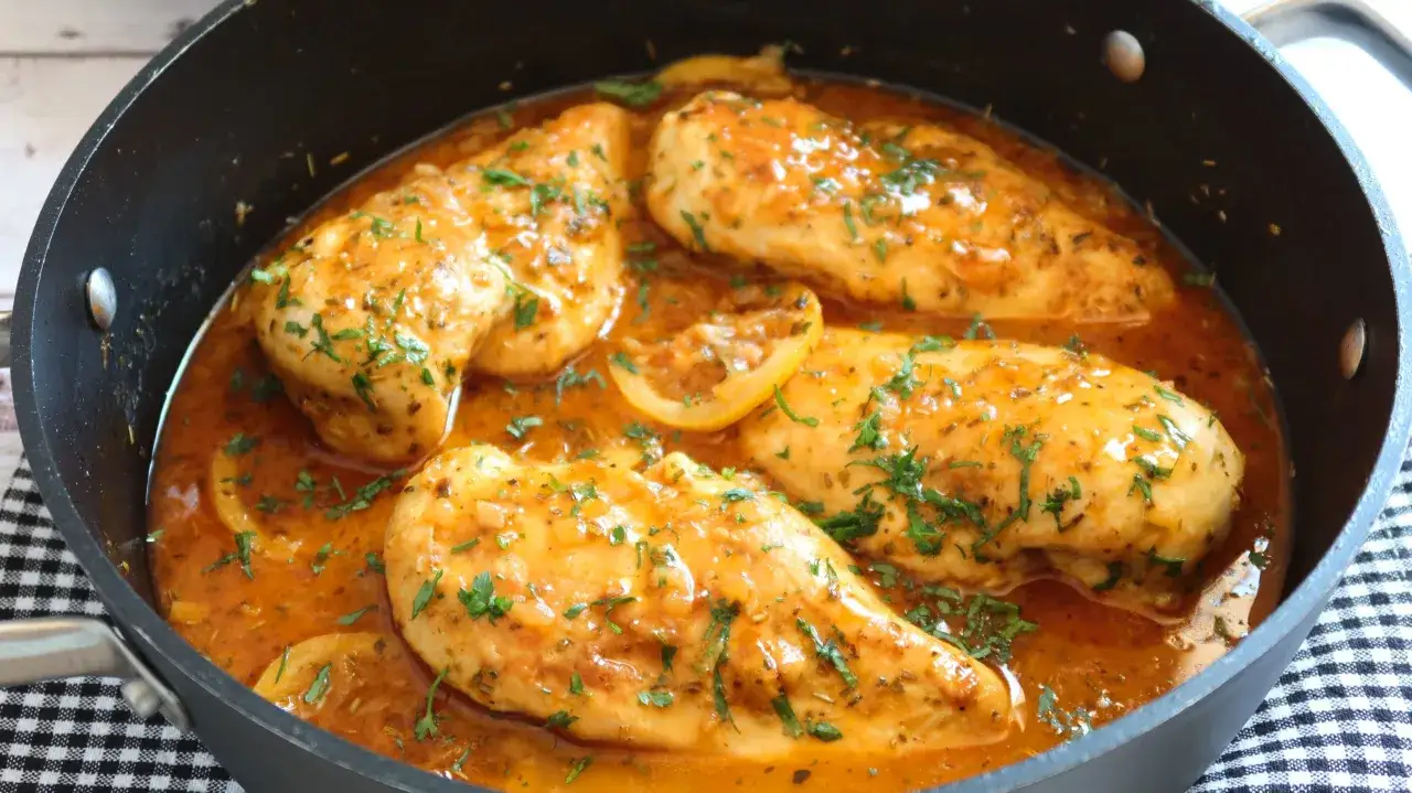 Sabroso pollo al lim&oacute;n en sart&eacute;n, ba&ntilde;ado en una salsa dorada y adornado con perejil fresco y rodajas de lim&oacute;n.
