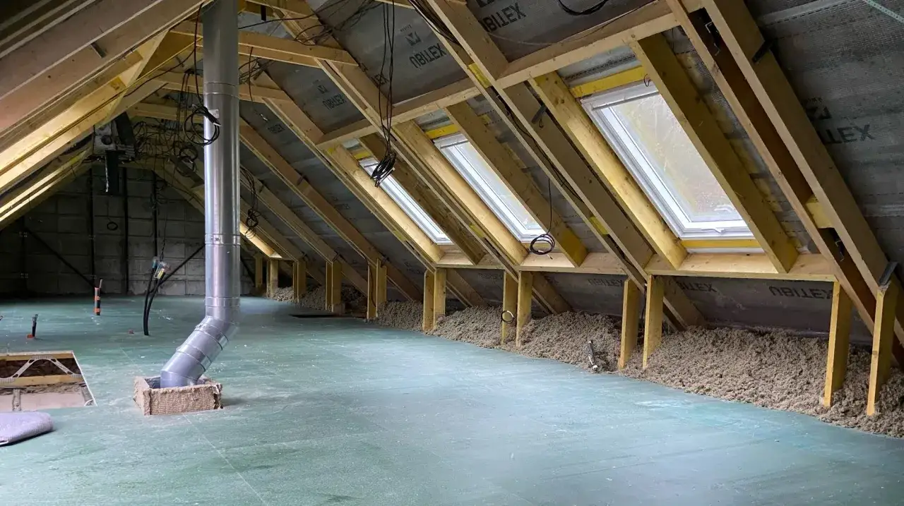Aménagement des combles d'une maison Phénix : charpente, fenêtres de toit, isolation et conduit de ventilation en cours.