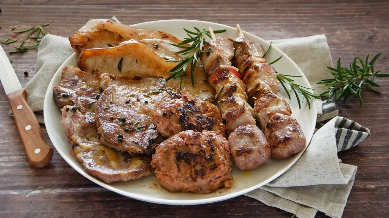 Un piatto invitante di grigliata di carne: costine, spiedini, salsicce e hamburger, guarniti con rosmarino fresco.