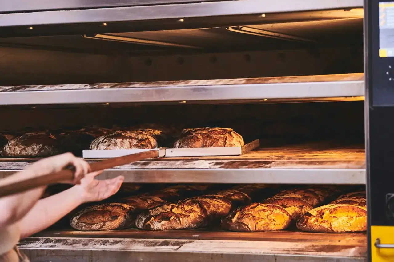 Bäcker holt frisches Brot aus dem Ofen. Hoffentlich ist die brotkruste zu hart, sonst schmeckt es nicht!