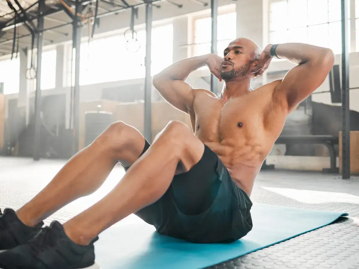 Man med träningskläder gör sit-ups på en blå matta i ett gym.