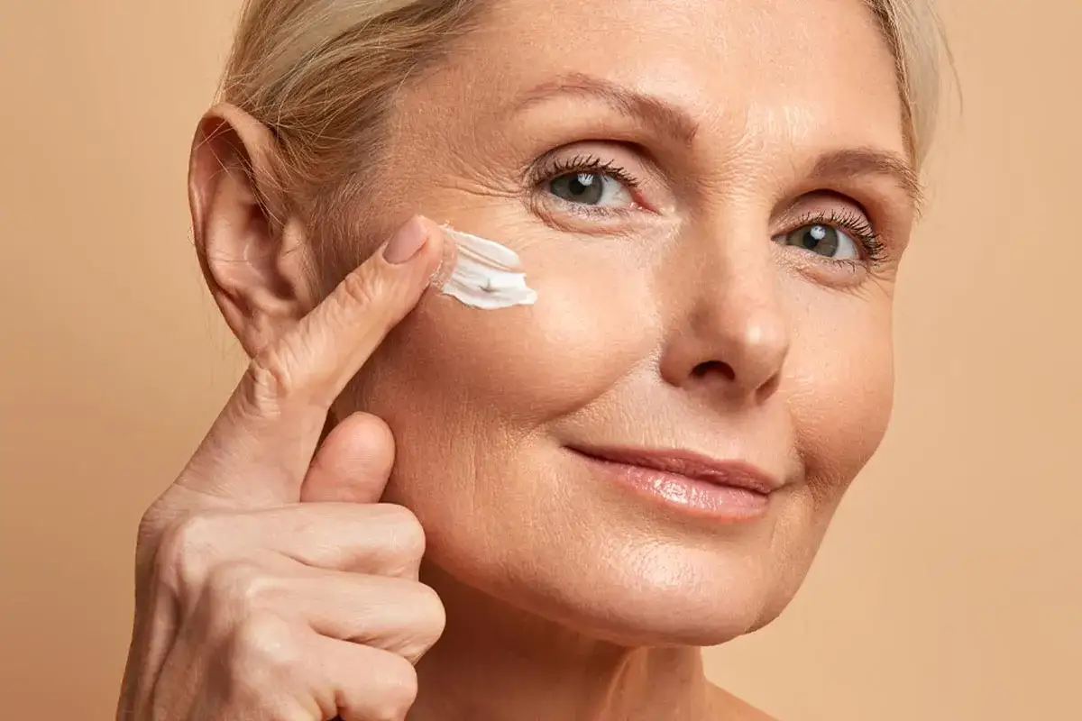 Donna applica crema sulla zona contorno occhi, un gesto di cura per la pelle matura.