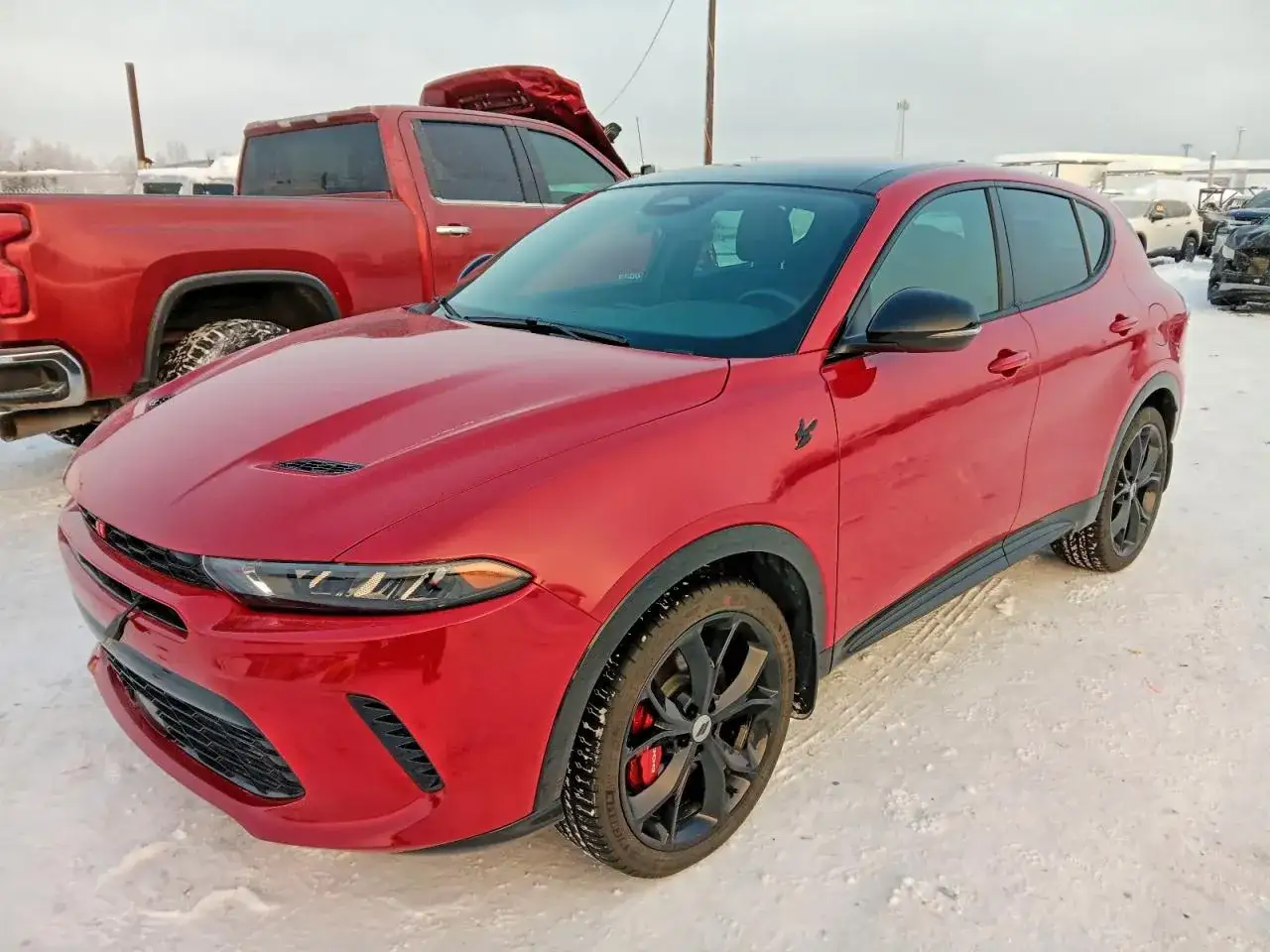 Czerwony Dodge SUV z czarnym dachem i felgami, zaparkowany na śniegu obok czerwonego pickupa.