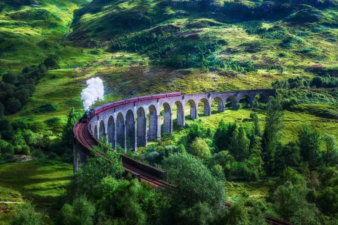 Malowniczy wiadukt Glenfinnan, gdzie kręcono sceny z Harry'ego Pottera, z pociągiem parowym na tle zielonych wzgórz Szkocji.