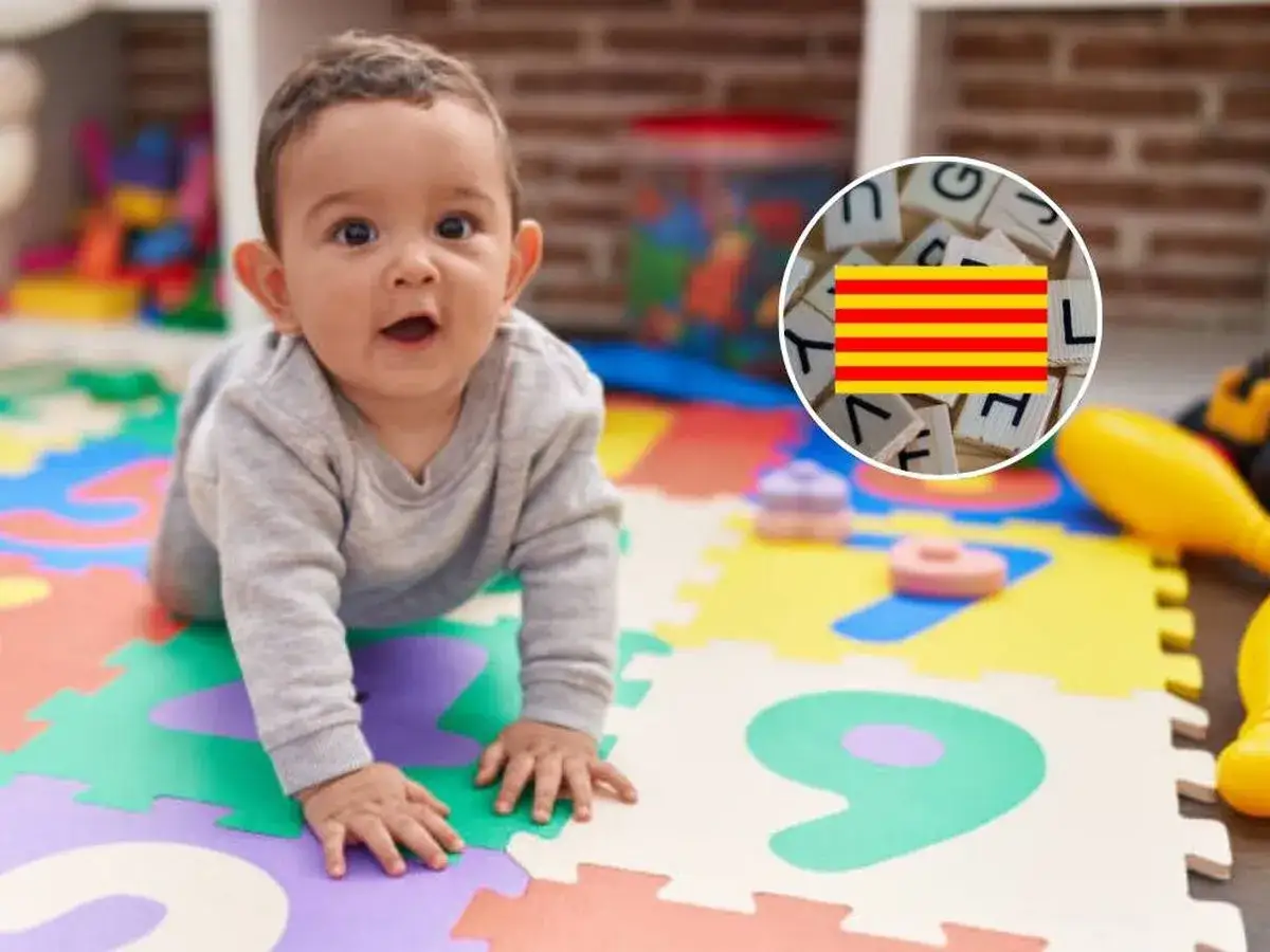 Bebé gateando sobre un tapete de números, con la bandera de Cataluña y letras de madera en un círculo.
