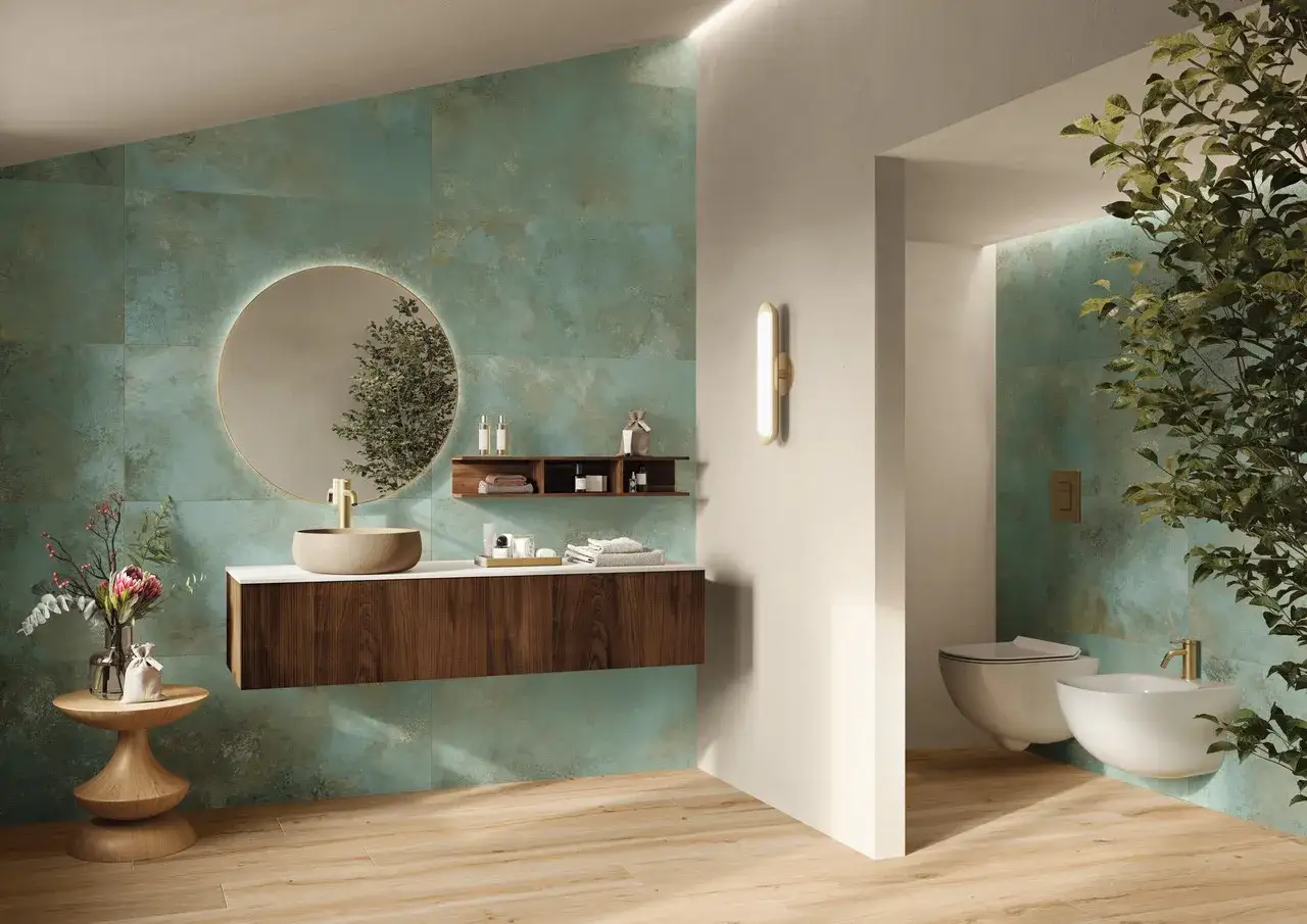 Elegante bagno verde petrolio e legno con lavabo in pietra, specchio rotondo e sanitari sospesi.