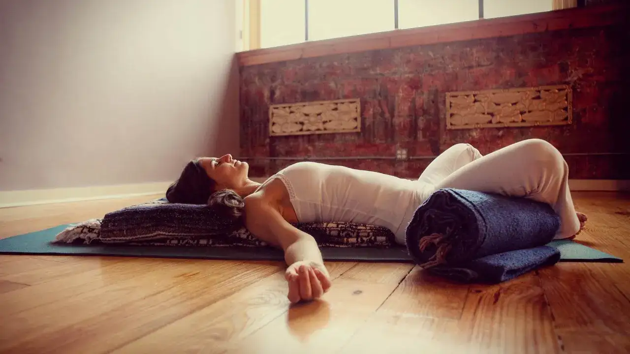 Kvinna i avslappnad position med en rullad filt som en **restorative yoga positioner** under knäna.