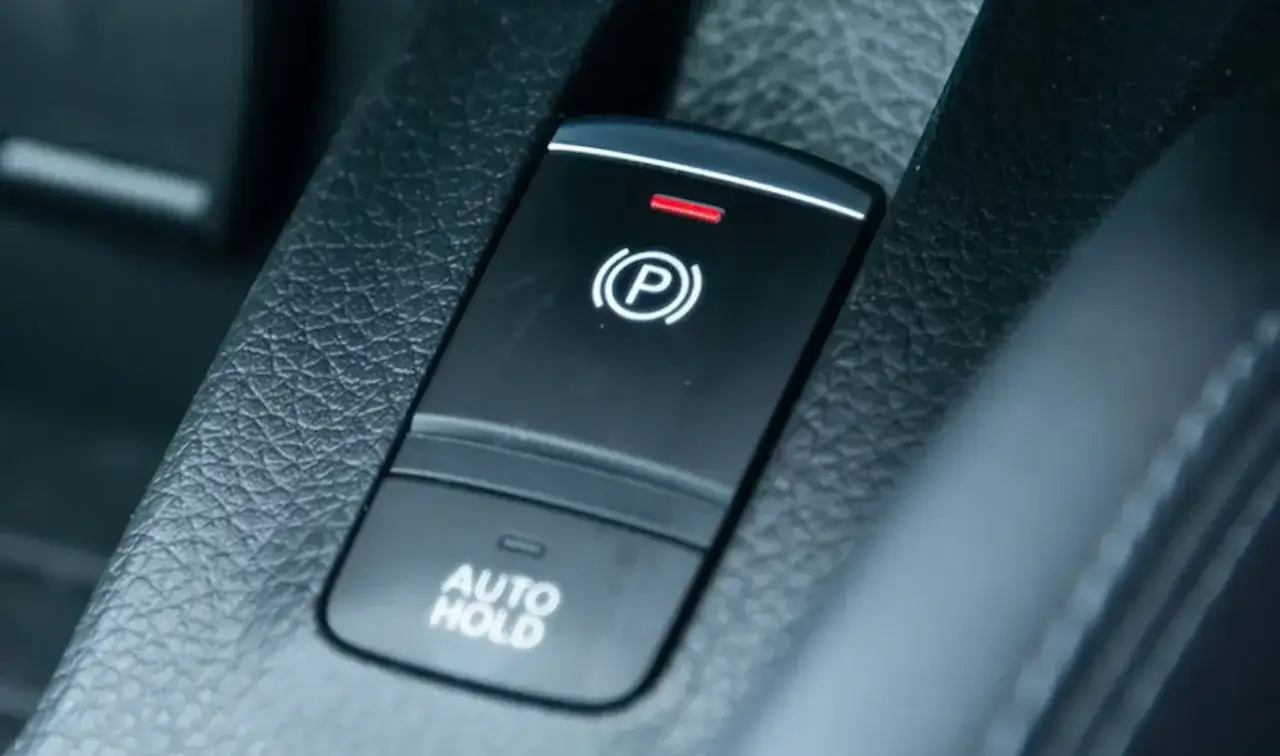 Przycisk hamulca ręcznego elektrycznego jak używać: naciśnij, by zaciągnąć, pociągnij, by zwolnić. Podświetlony symbol 