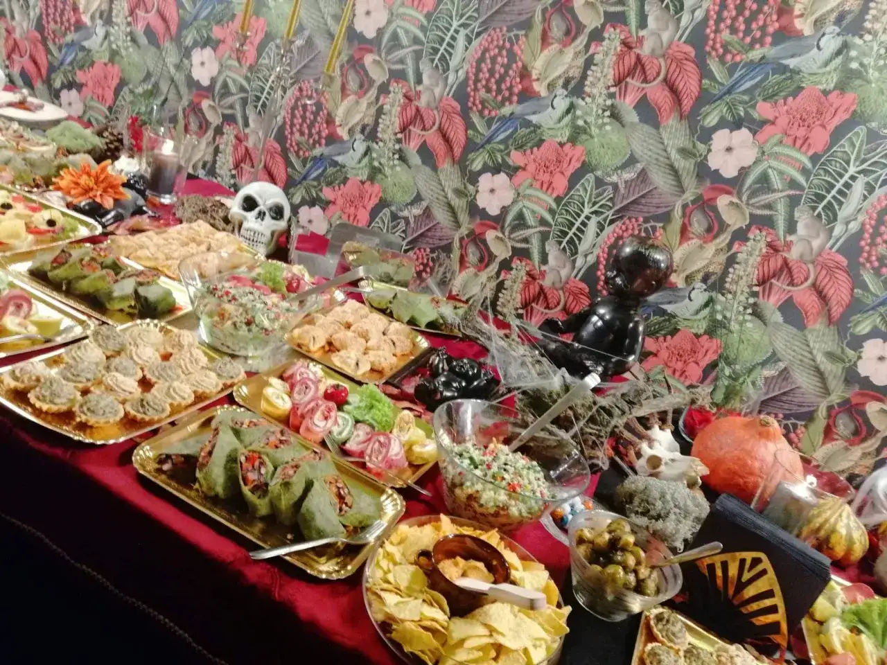 Stół z przekąskami, na którym widać m.in. roladki, tartaletki, chipsy i oliwki. W tle ozdoby halloweenowe, jak czaszka i dynia. Pan kanapka łódź mógłby się tu poczuć jak w raju!