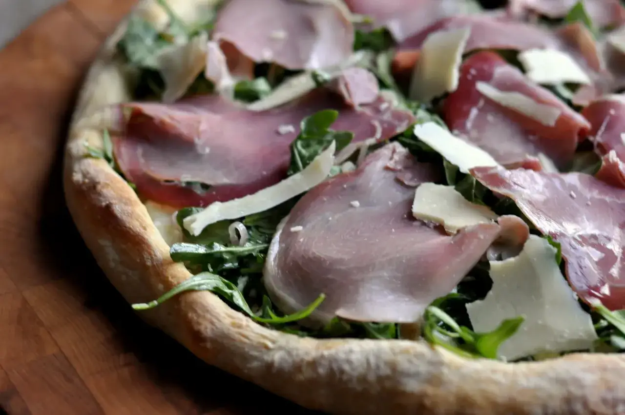En uts&ouml;kt pizza bianco med tunna skivor parmaskinka, f&auml;rsk ruccola och hyvlad parmesanost.