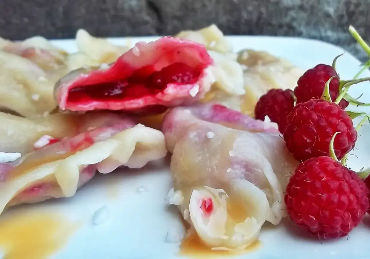 Pyszne pierogi z malinami, z soczystym, czerwonym nadzieniem i świeżymi malinami na talerzu.