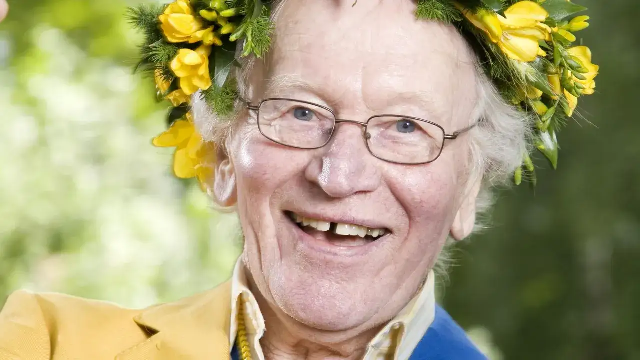 Glad Britt Skogman med blomsterkrans och glasögon ler mot kameran.