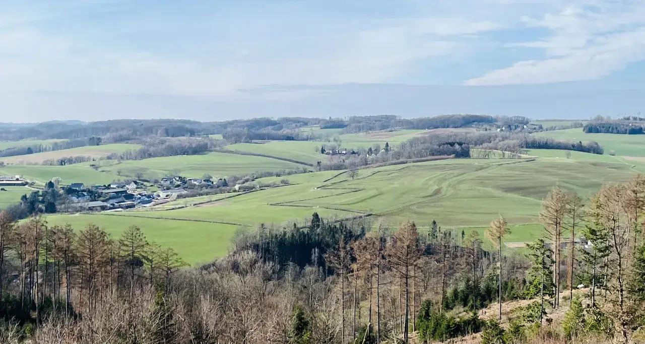 Weite grüne Hügel und Felder bei Lindlar, mit einem kleinen Dorf im Tal. Der Metabolon Lindlar ist Teil dieser idyllischen Landschaft.