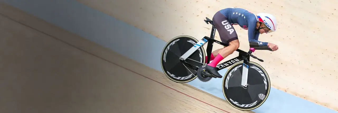 A determined track cyclist in a USA kit races on a wooden velodrome, pushing hard for victory.