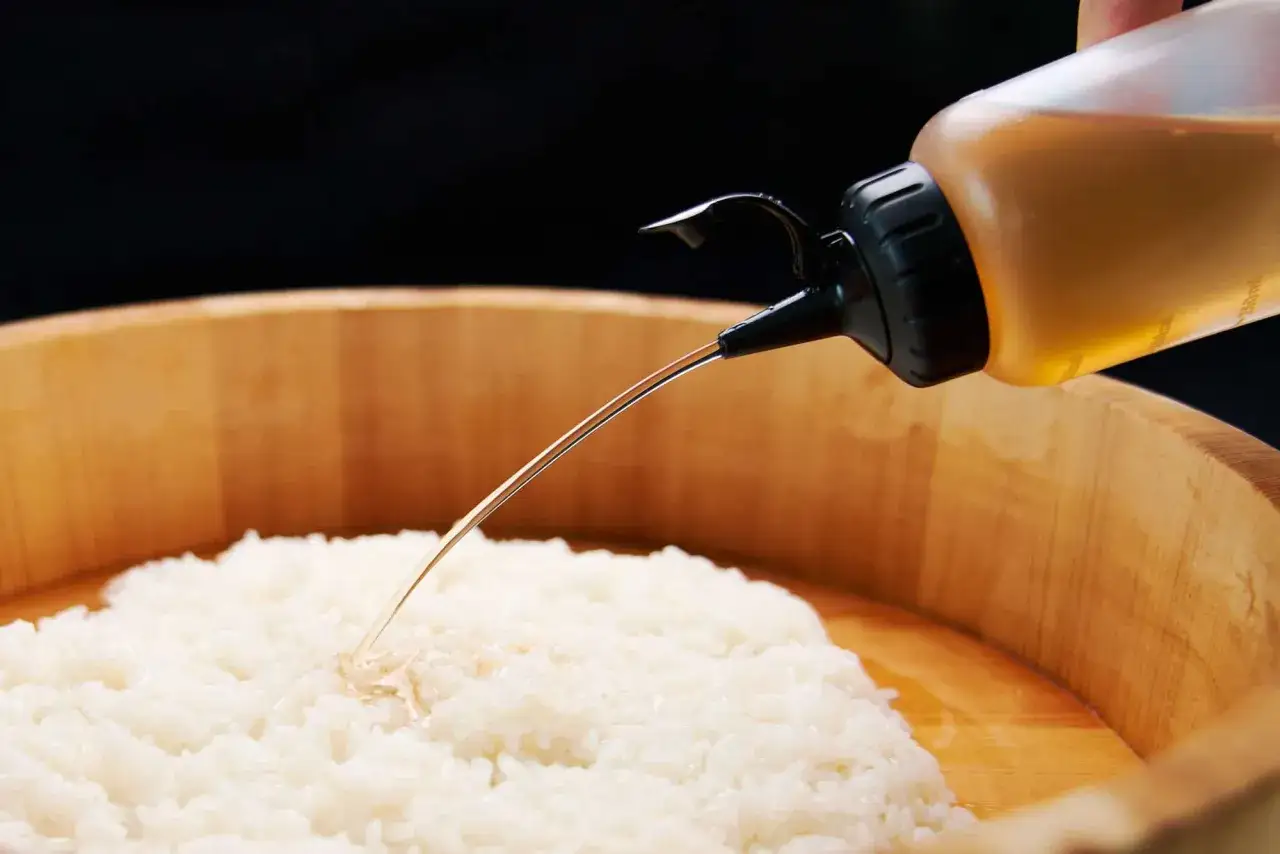 Polewanie ryżu do sushi octem ryżowym z butelki.
