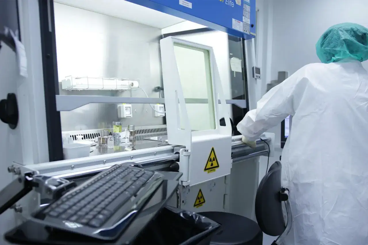 Pracownik w kombinezonie ochronnym pracuje przy aparaturze z symbolem promieniowania. To pokazuje, jak chronić się przed promieniowaniem jądrowym w laboratorium.