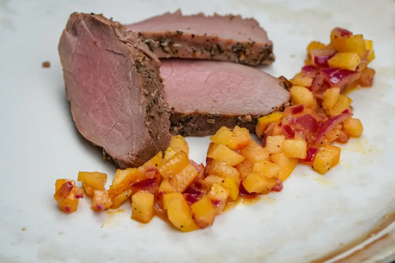 Tranches de filet de porc fumé, tendres et juteuses, accompagnées d'une compotée colorée de fruits et d'oignons rouges.