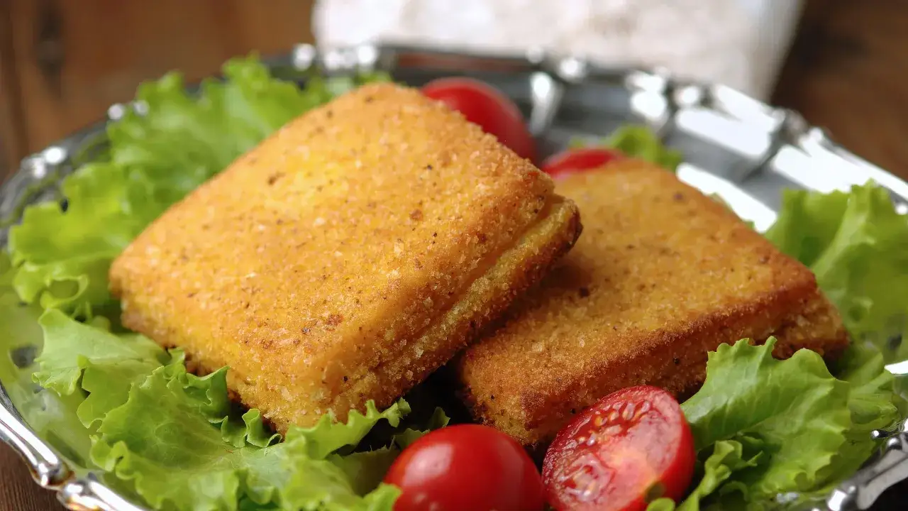 Due croccanti mozzarella in carrozza in friggitrice ad aria, servite su un letto di lattuga con pomodorini.