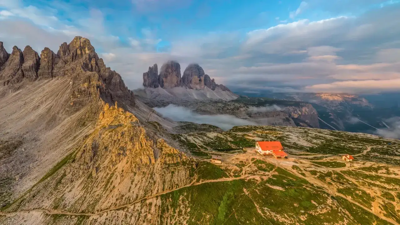 Majestueuses montagnes des Dolomites en Italie, avec un refuge rouge et des nuages bas.