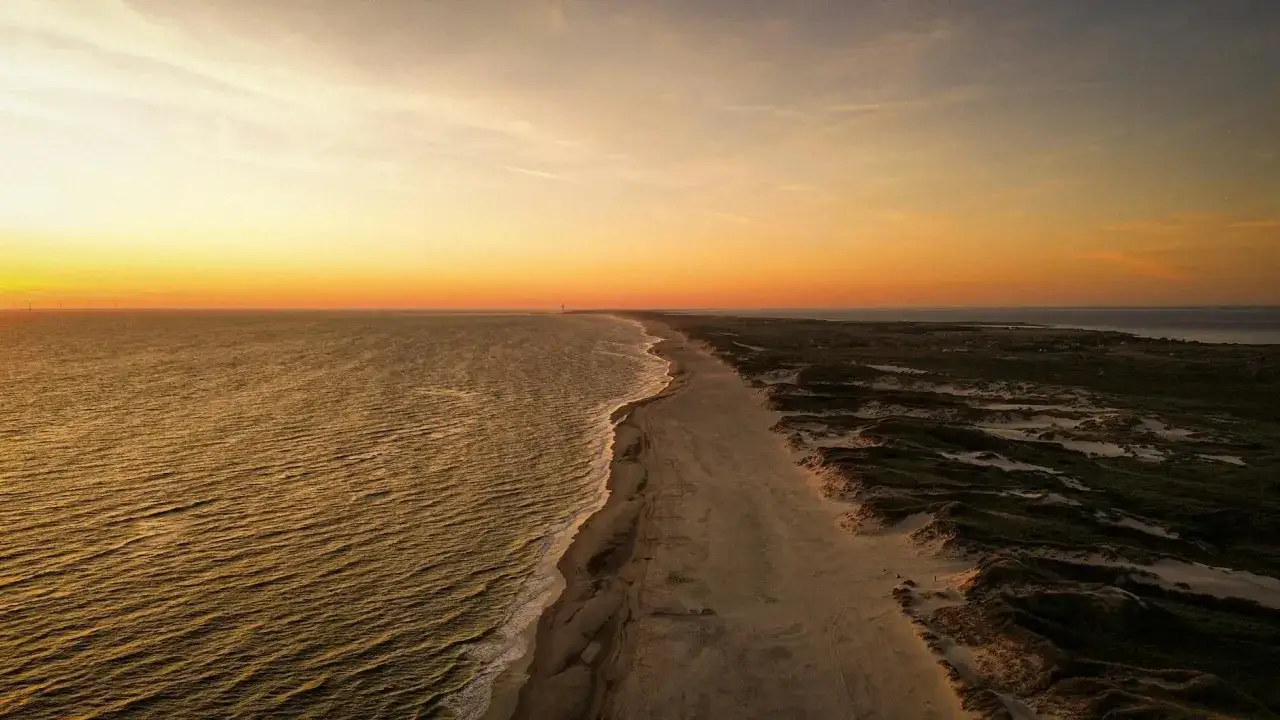 Zachód słońca nad morzem, piaszczysta plaża i wydmy tworzą malowniczą scenerię. Dziwnów promenada w oddali.